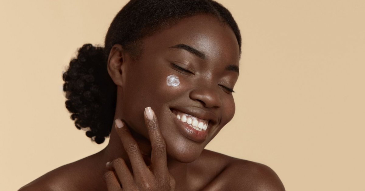 Femme noire souriante appliquant une crème sur son visage